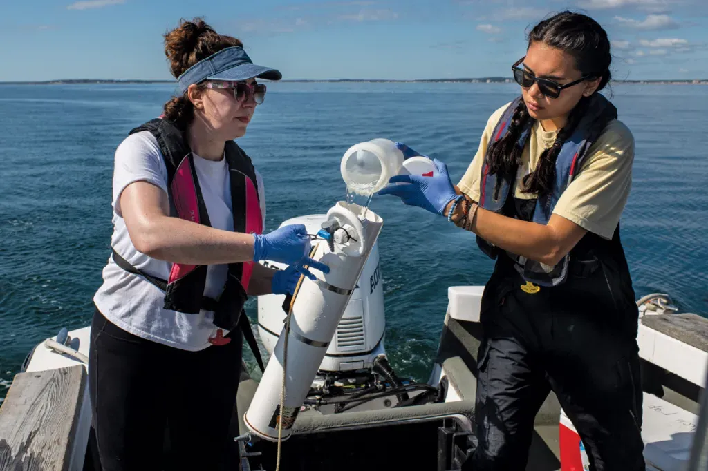 Two marine science students filling a sampling container with ocean water